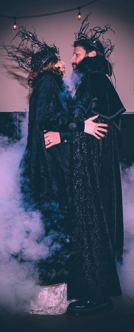 Sean and Bethany embracing in black cloaks and crowns of twisted branches, fog swirling around them